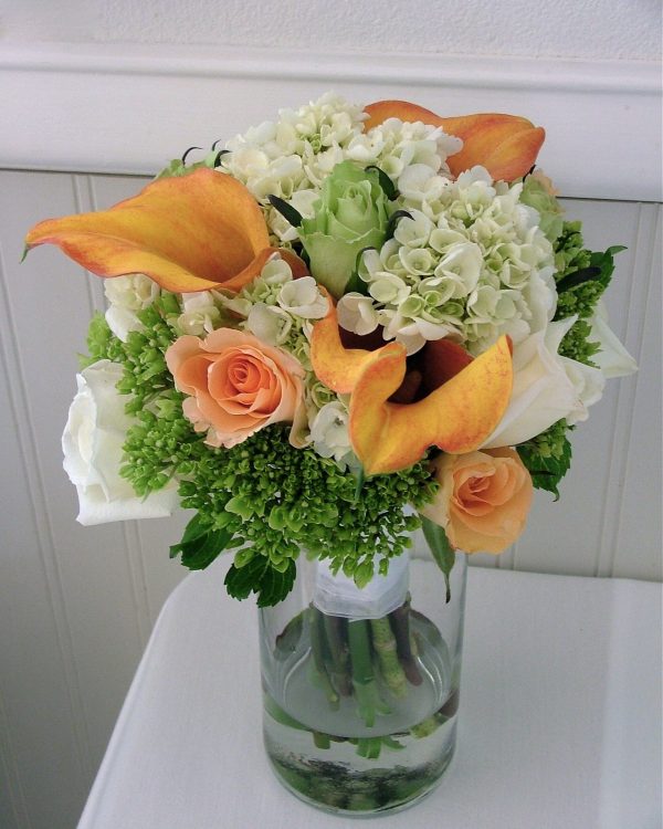 A bouquet of peach roses, orange callas and green hydrangea in a vase